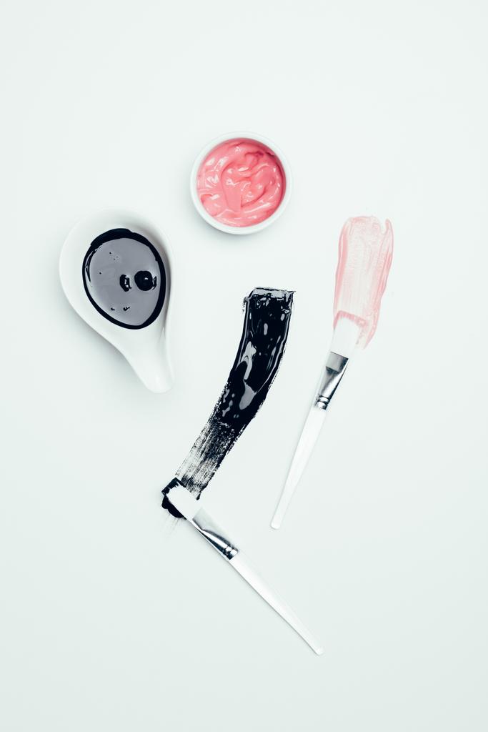 vista superior de máscaras, manchas y cepillos negros y rosados aislados en la superficie blanca
 - Foto, imagen