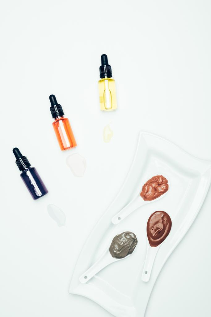 bovenaanzicht van klei poeder, cosmetische flessen met pijpen, plaat en lepels met verschillende kleurrijke klei masker geïsoleerd op wit oppervlak  - Foto, afbeelding