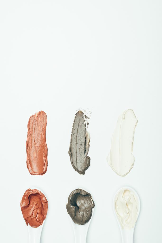επίπεδη lay με κουτάλια και διάφορα πολύχρωμα άργιλος μάσκα μουτζούρες απομονώνονται σε λευκή επιφάνεια  - Φωτογραφία, εικόνα