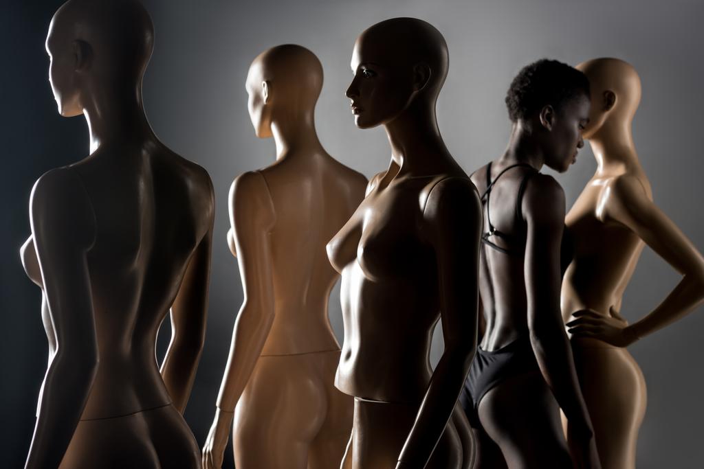 молода афроамериканка в боді-костюмі, що стоїть між манекенами на чорному
   - Фото, зображення