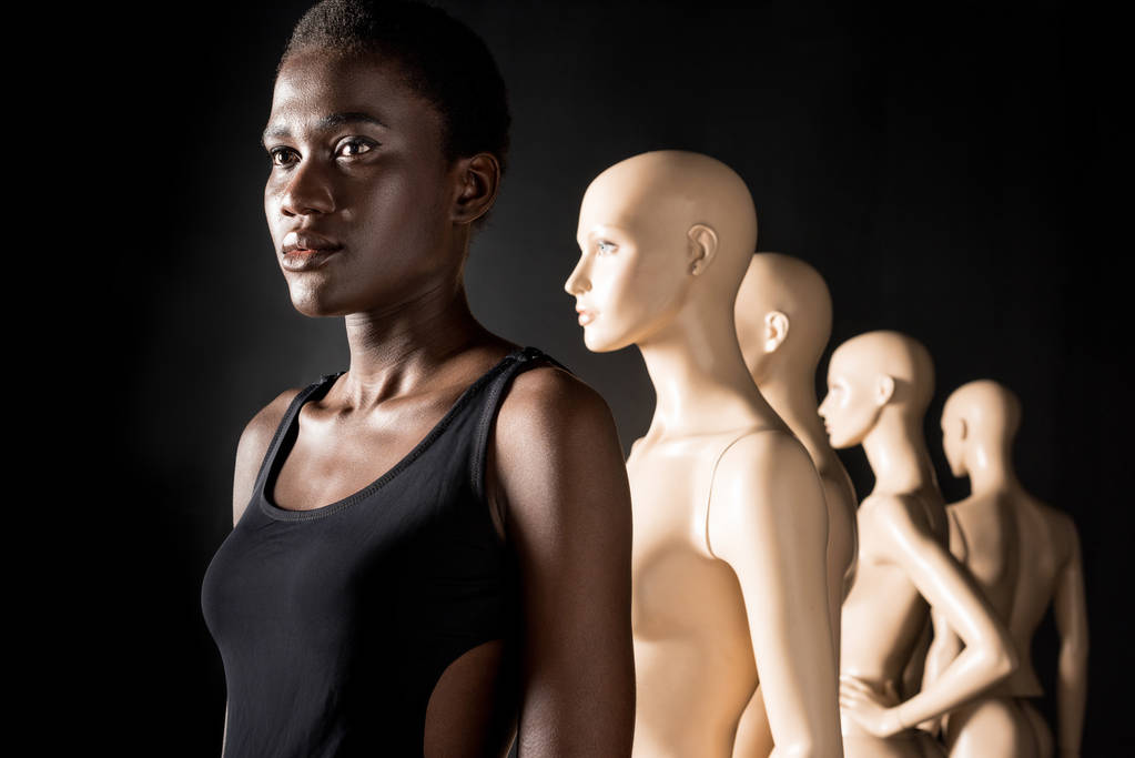afrikanisch-amerikanisches Mädchen steht mit Schaufensterpuppen in der Reihe und schaut weg auf schwarz - Foto, Bild
