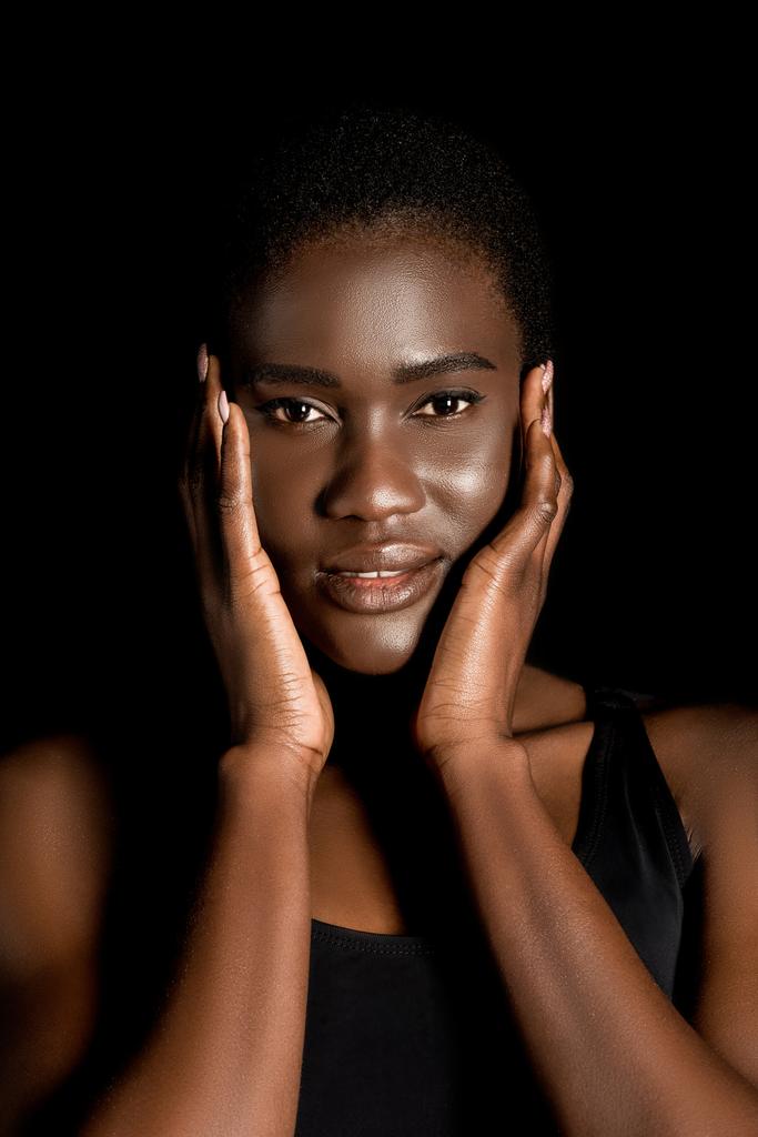 szép afro-amerikai nő megérintette az arcát, kezét és mosolyogva elszigetelt fekete kamera portréja - Fotó, kép