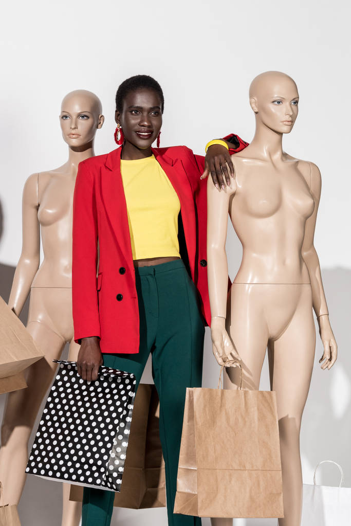 красивая улыбающаяся африканская американка, стоящая между манекенами с пакетами покупок на белом
  - Фото, изображение