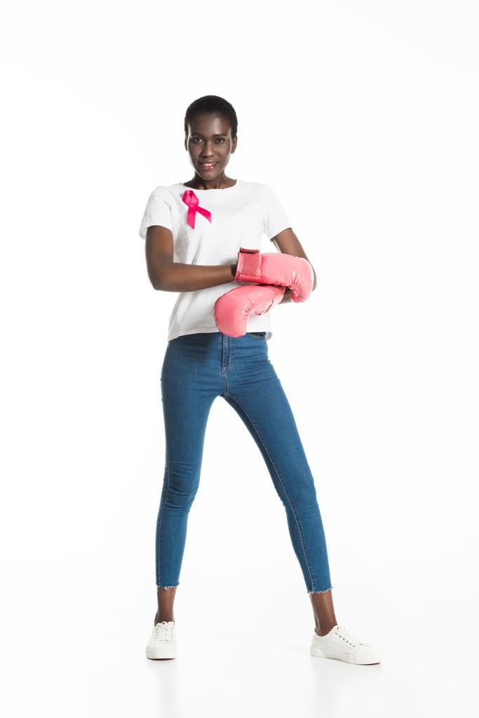 vue pleine longueur de la jeune femme avec ruban rose portant des gants de boxe et souriant à la caméra isolé sur blanc, concept de cancer du sein
 - Photo, image