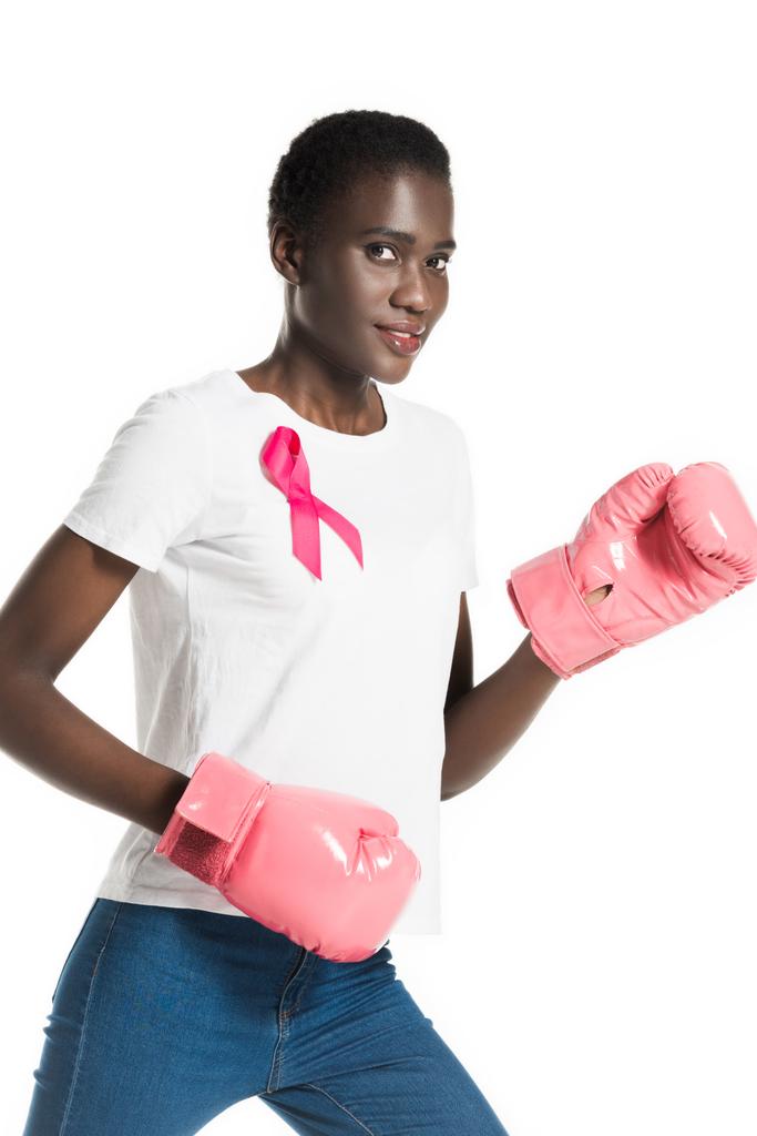 Вид сбоку на молодую женщину с розовой лентой на футболке боксера и улыбкой перед камерой, изолированной на белом, концепция рака груди
 - Фото, изображение