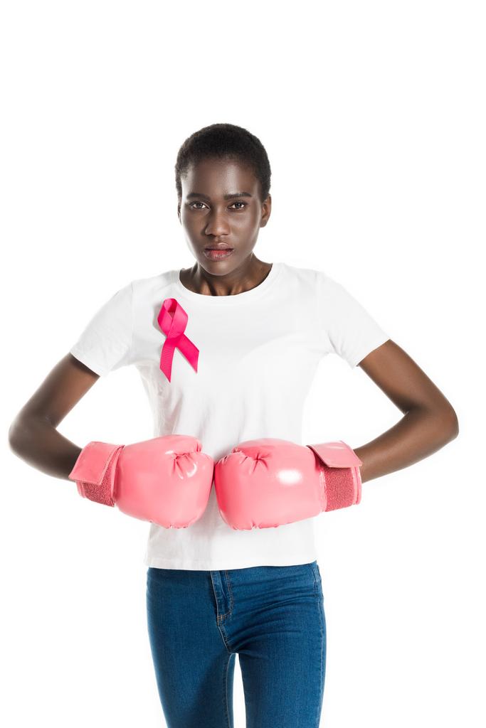 mladá žena s růžovou stuhou na tričku nosí Boxerské rukavice a při pohledu na fotoaparát, samostatný stromovité bílý, rakovina prsu - Fotografie, Obrázek