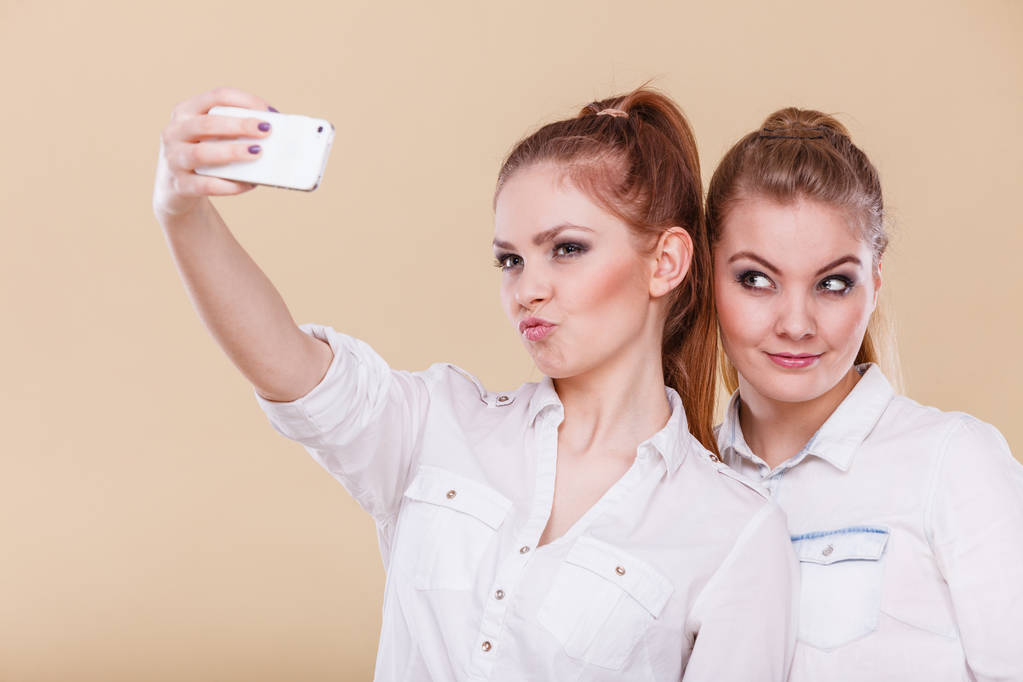 Divertido conceito de selfie de ligação. Irmãs ou melhores amigos, duas meninas loiras estudante tirando auto foto com câmera de telefone inteligente, se divertindo, emoção engraçada positiva no rosto
 - Foto, Imagem