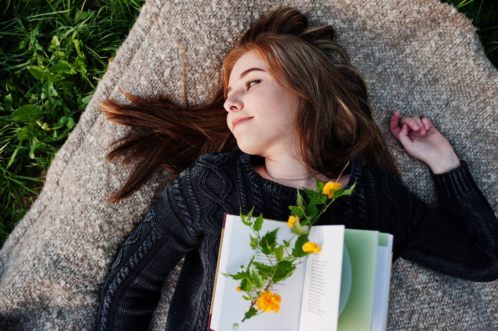 Jonge brunette meisje liggend op plaid met boek. - Foto, afbeelding