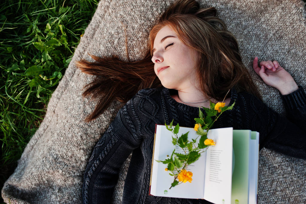 Giovane ragazza bruna sdraiata su plaid con libro
. - Foto, immagini