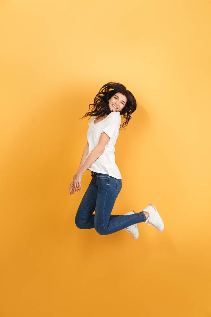 Image of young emotional woman jumping isolated over yellow background. Looking camera. - Photo, Image