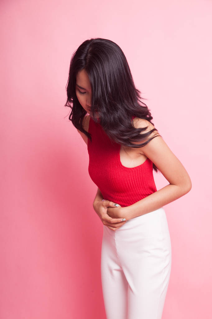 Pembe arka planda genç Asyalı kadının karnı ağrıyor. - Fotoğraf, Görsel