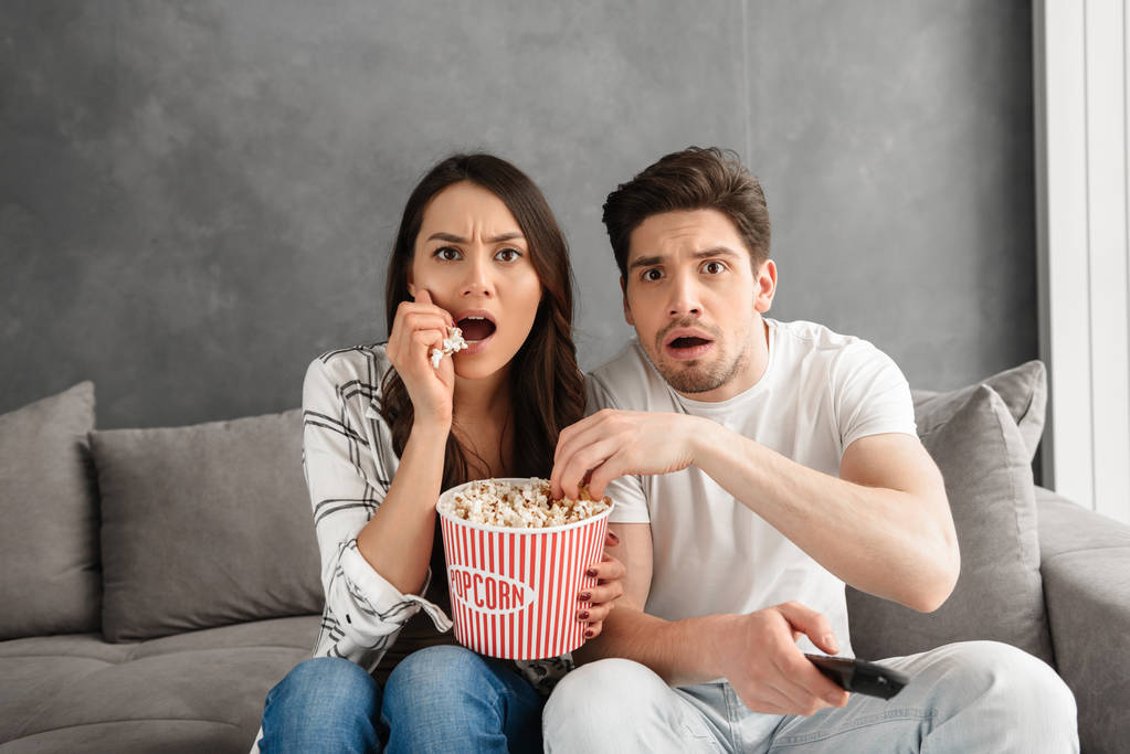 Зображення тривожної сім'ї, що сидить на дивані вдома і дивиться на тебе, дивлячись страшний фільм і їдячи попкорн
 - Фото, зображення