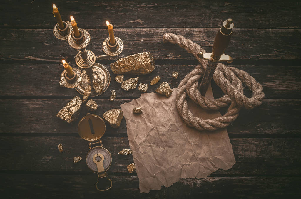 Pirate gold and treasure map crumpled parchment with copy space, dagger, compass and ship rope on old table background. - Photo, Image