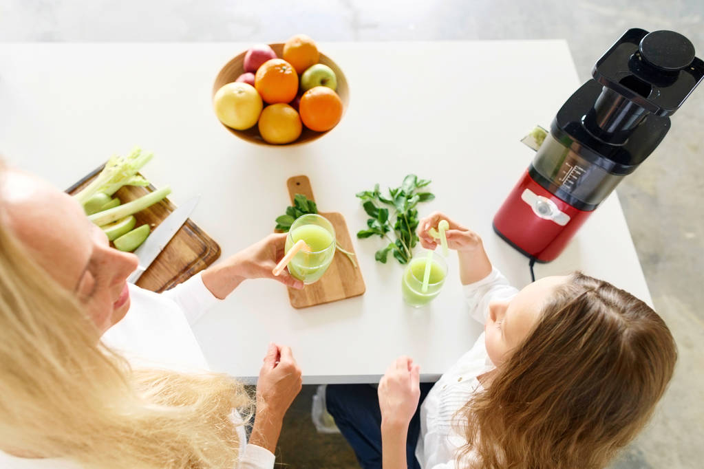 Pojęcie zdrowego stylu życia. Ładna dziewczynka i jej matka napój zdrowy napój z seler, jabłko, mięty i uśmiechając się w kuchni w domu widok z góry - Zdjęcie, obraz