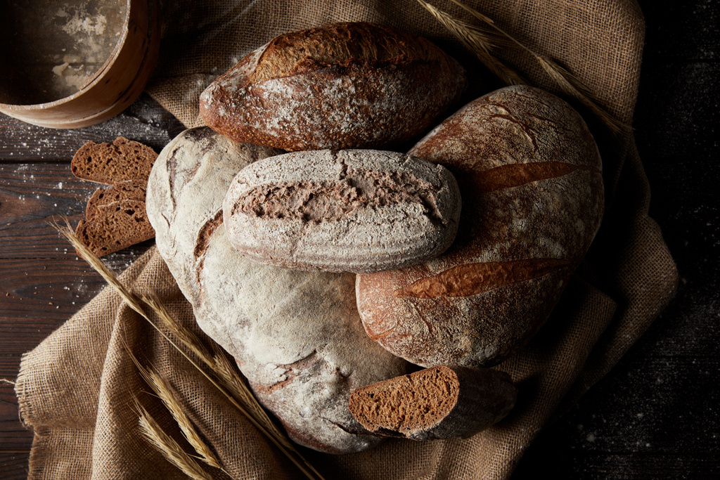 vista elevada de vários tipos de pão, trigo, peneira e saco na mesa de madeira
  - Foto, Imagem