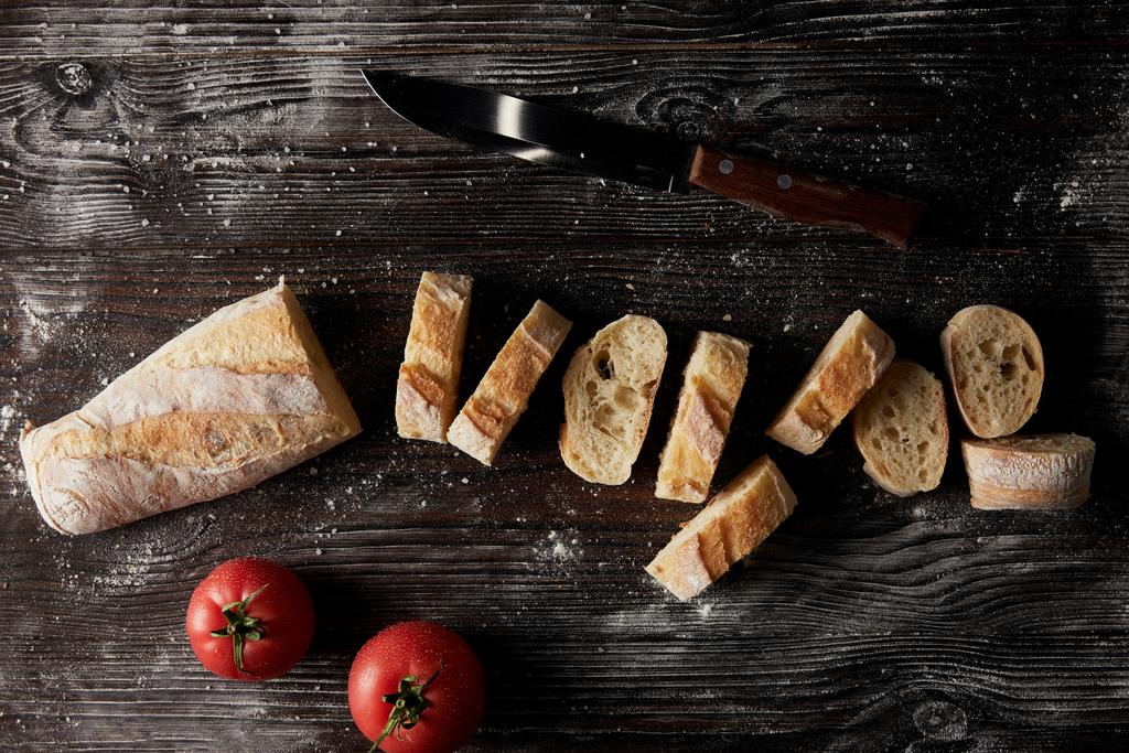 vista superior de fatias de baguete, tomates e faca na mesa de madeira que cobre pela farinha
  - Foto, Imagem