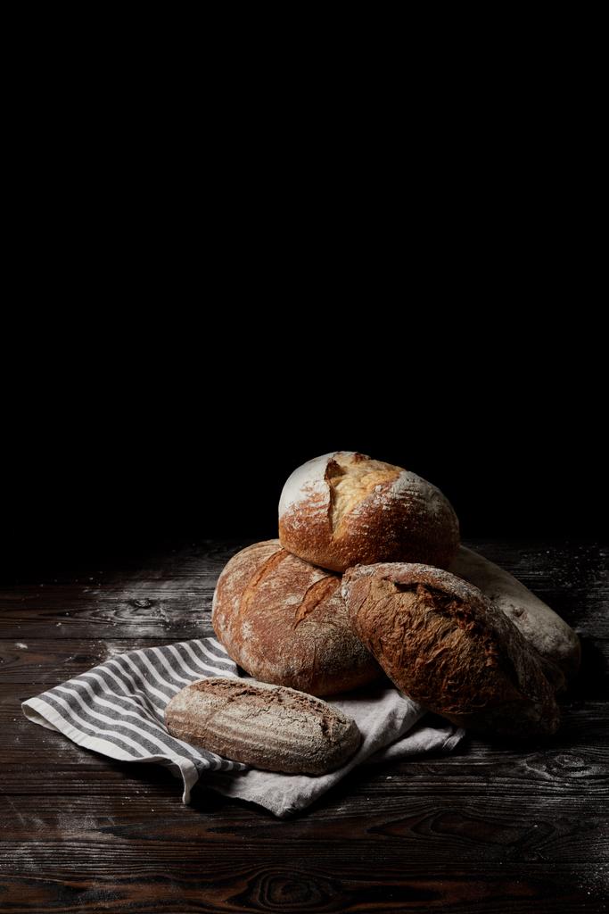 Detailní pohled různých druhů chleba a žíně na dřevěný stůl podkladě mouky izolovaných na černém pozadí - Fotografie, Obrázek