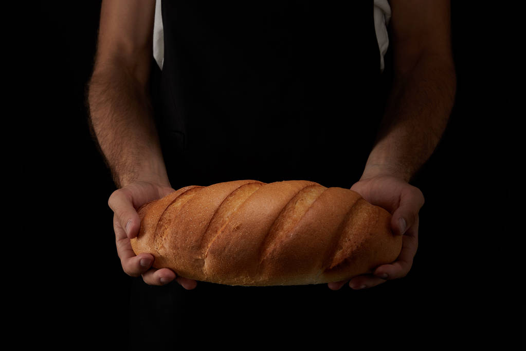 cropped image of male baker in apron holding bread isolated on black background  - Photo, Image