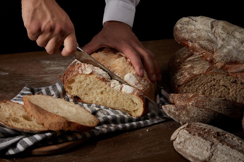 tiro recortado de panadero masculino cortar pan por cuchillo en tela de saco en la mesa de madera
 - Foto, imagen