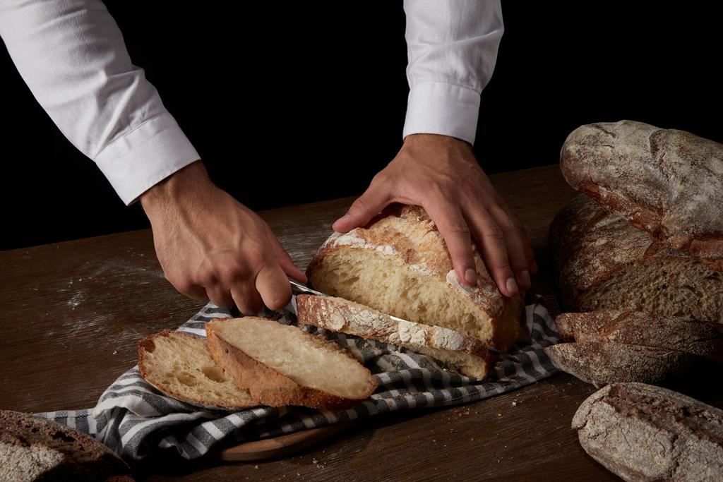 részleges kilátás férfi baker vágás kenyér késsel a zsákvászon, a fából készült asztal - Fotó, kép