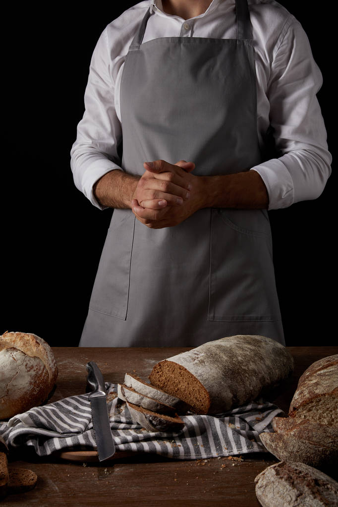 Schnappschuss eines Bäckers in Schürze, der neben Tisch mit Messer, Sacktuch und Brot steht  - Foto, Bild