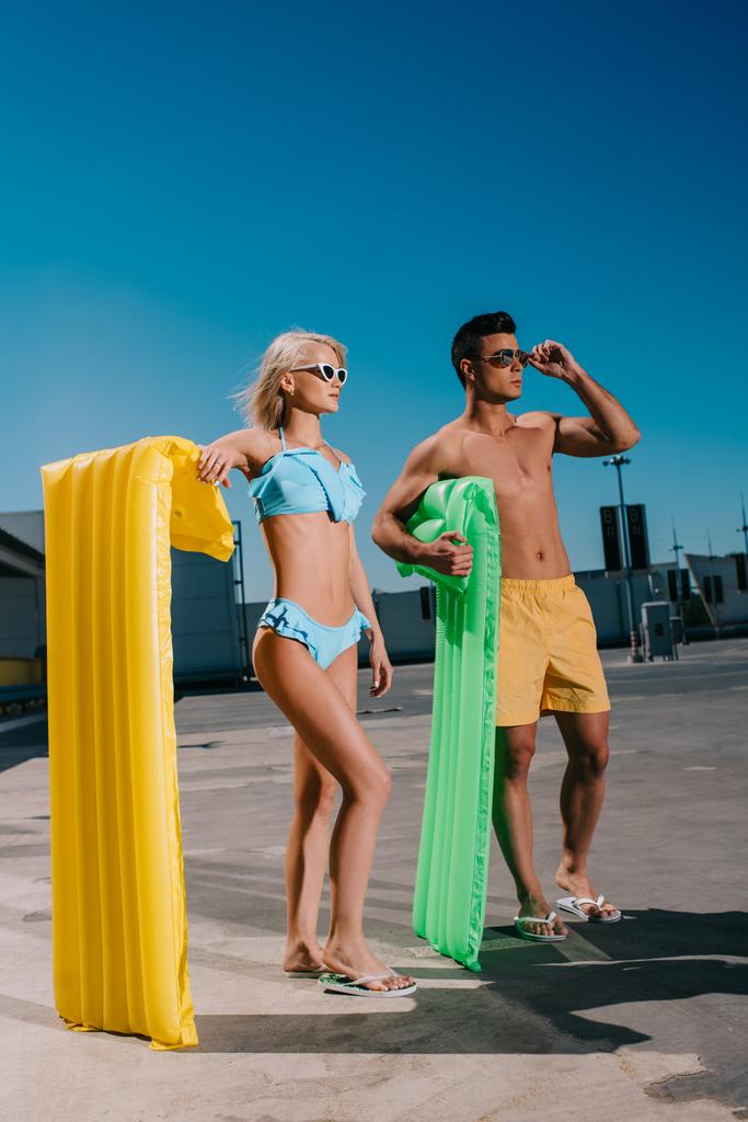 jeune couple en vêtements de plage avec lits gonflables debout sur le parking
 - Photo, image