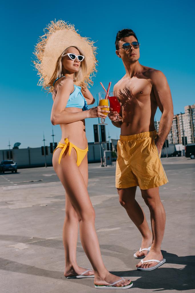 atractiva pareja joven en ropa de playa con refrescantes cócteles de pie en el aparcamiento
 - Foto, imagen