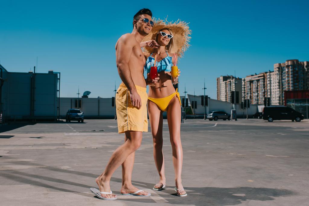 pareja joven en ropa de playa con refrescantes cócteles de pie en el aparcamiento
 - Foto, imagen