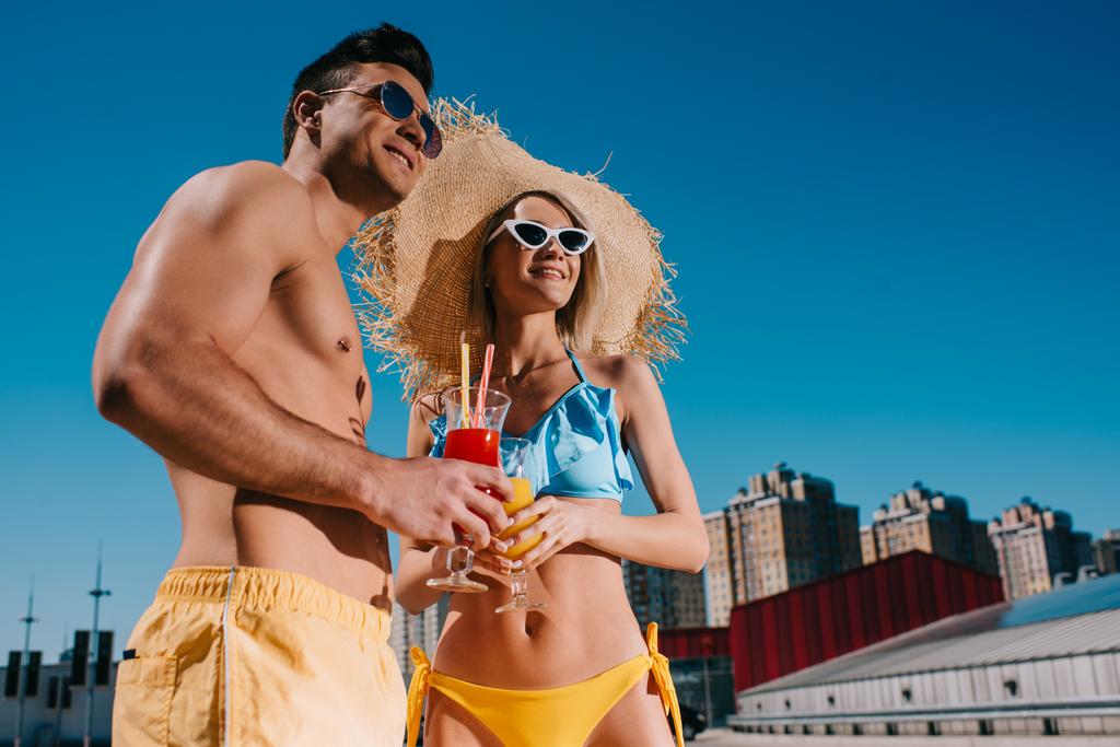 bottom view of young couple in swimsuits with refreshing cocktails in city - Photo, Image