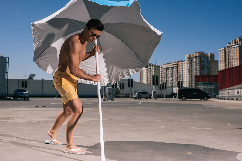 attractive young man putting beach umbrella in asphalt on parking - Photo, Image