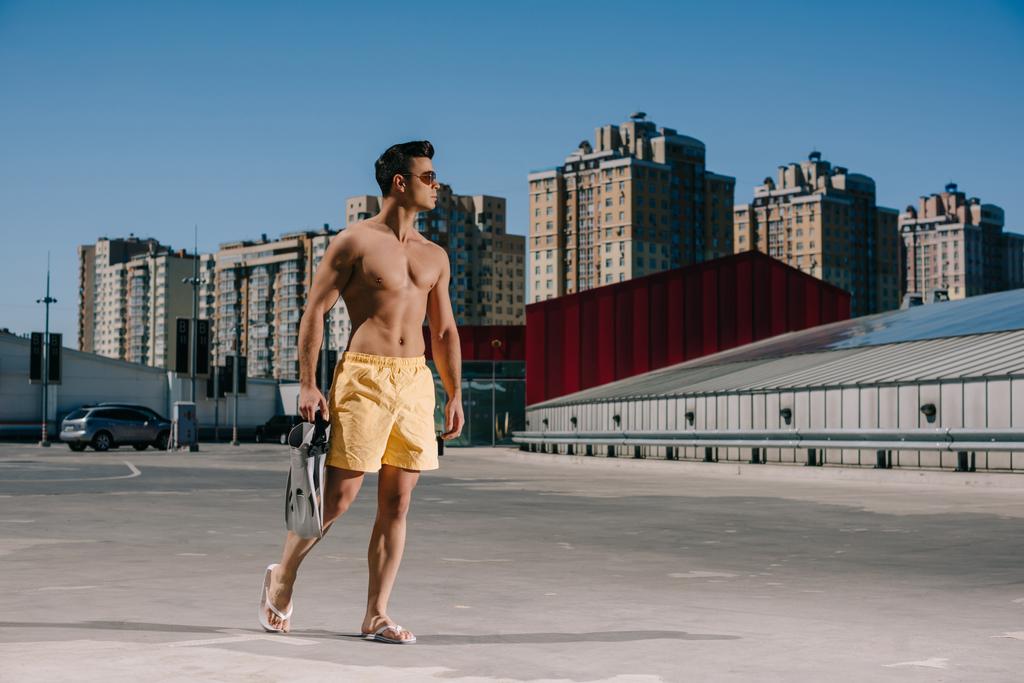 guapo joven sin camisa hombre en pantalones cortos de natación con aletas en el aparcamiento
 - Foto, Imagen