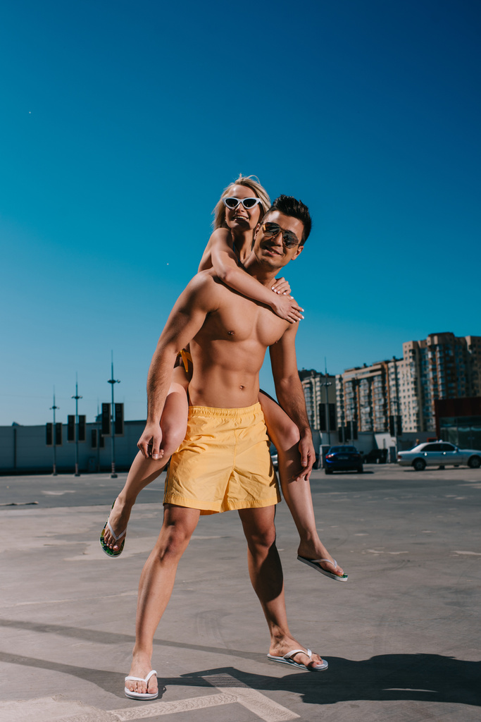 jovem atraente mulher piggybacking no namorado no estacionamento
 - Foto, Imagem