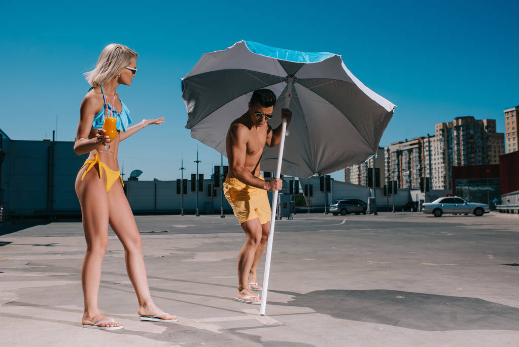 mladý pár s deštníkem v plavky opalování na parkování - Fotografie, Obrázek