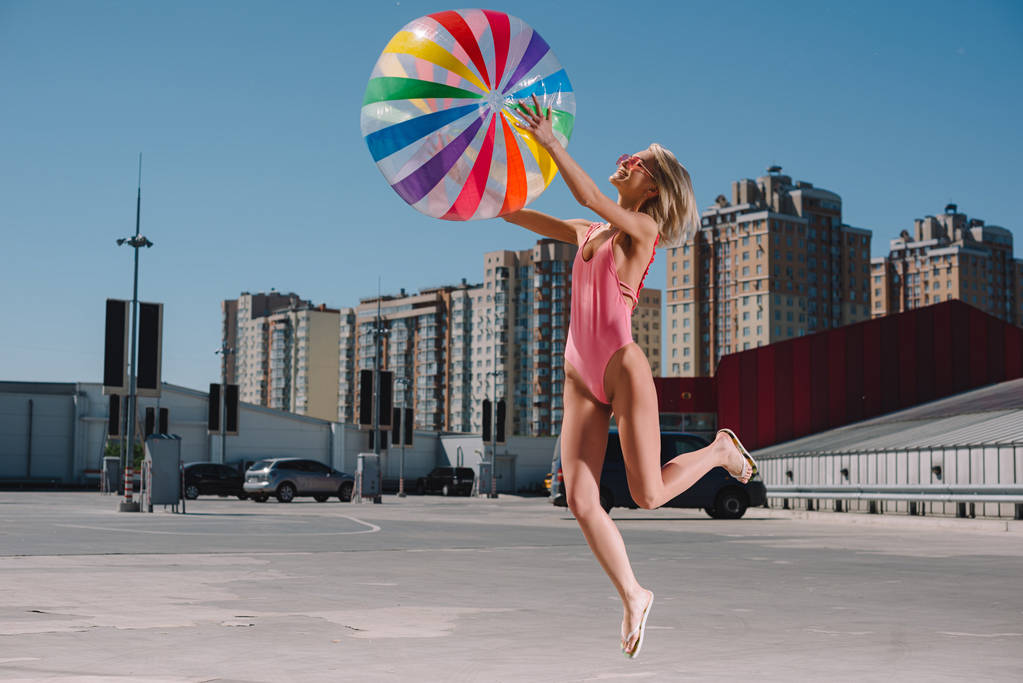 красивая молодая женщина в купальниках прыгает с красочным пляжным мячом на парковке
 - Фото, изображение
