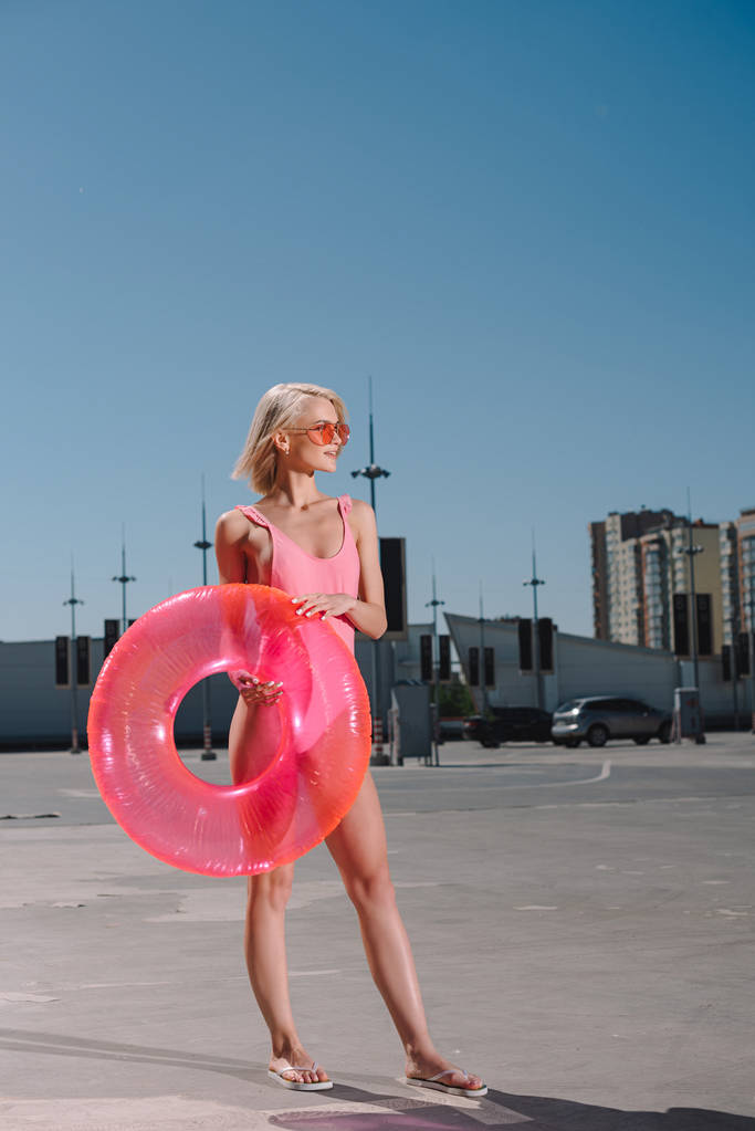 young woman in stylish pink swimsuit with inflatable ring on parking - Photo, Image