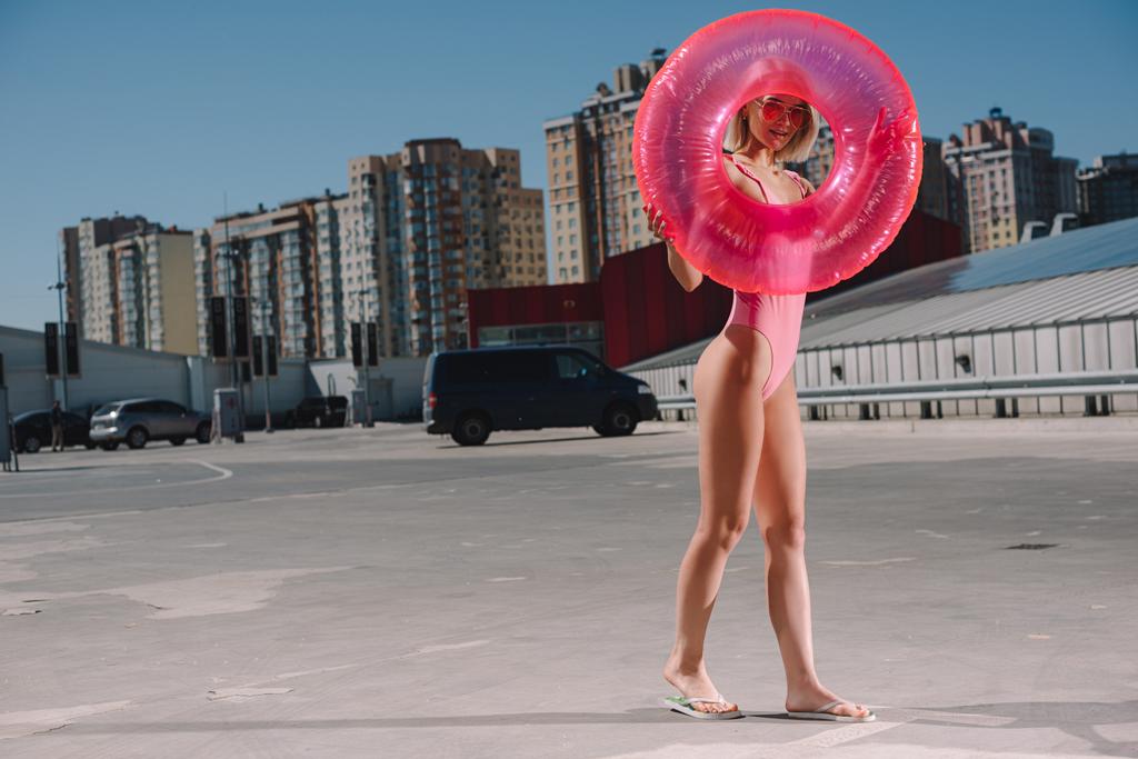 attraktive junge Frau im Badeanzug mit aufblasbarem Ring auf dem Parkplatz - Foto, Bild