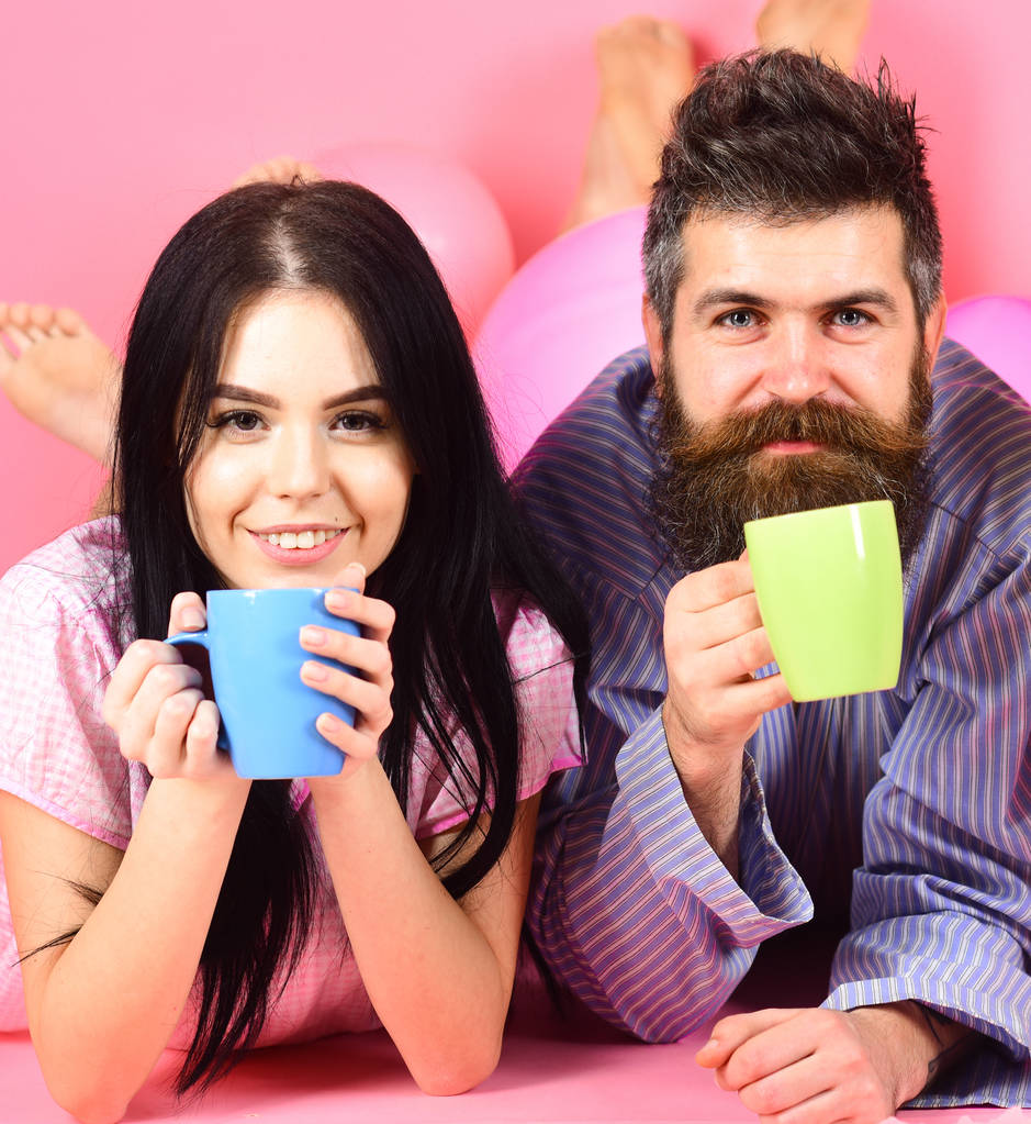 Couple relax in morning with coffee. Family tradition concept. Man and woman on smiling faces lay, pink background. Couple in love drink coffee in bed. Man and woman in domestic clothes, pajamas - Photo, Image