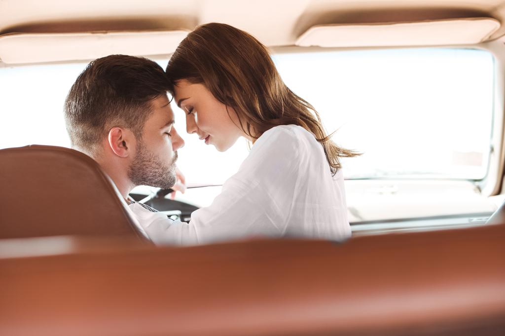 beautiful couple with closed eyes going to kiss in car together - Photo, Image