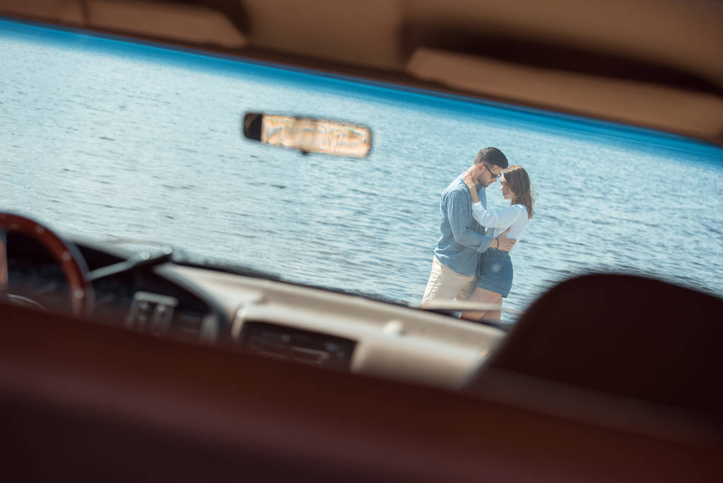 joven pareja de viajeros abrazando cerca del mar, vista a través de coche
 - Foto, Imagen