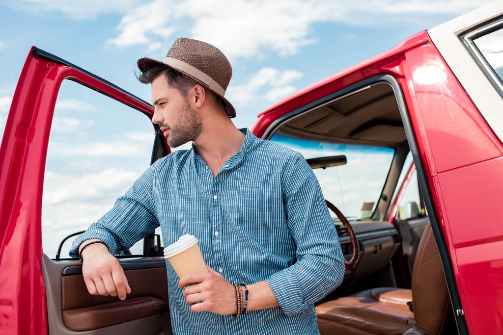 道路の旅行中に車でコーヒーの立っている使い捨てカップを持つスタイリッシュな男 - 写真・画像