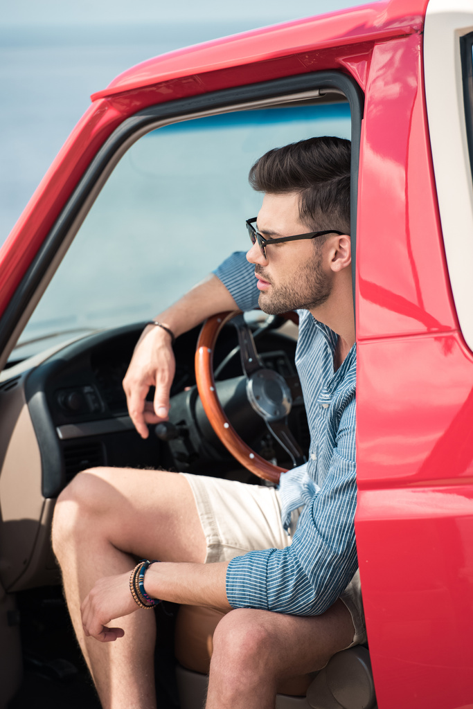 knappe jongeman in zonnebril zitten in rode auto - Foto, afbeelding