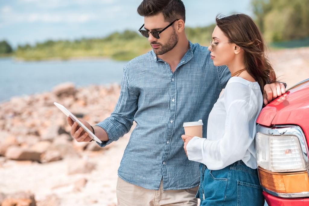 мужчина с чашкой кофе и девушка с помощью цифровой планшет возле автомобиля, дорожное путешествие
 - Фото, изображение