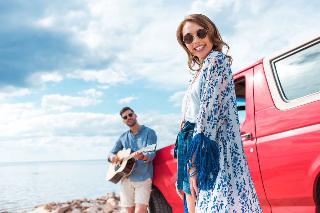 jovem tocando guitarra acústica perto do carro com namorada sorridente
 - Foto, Imagem