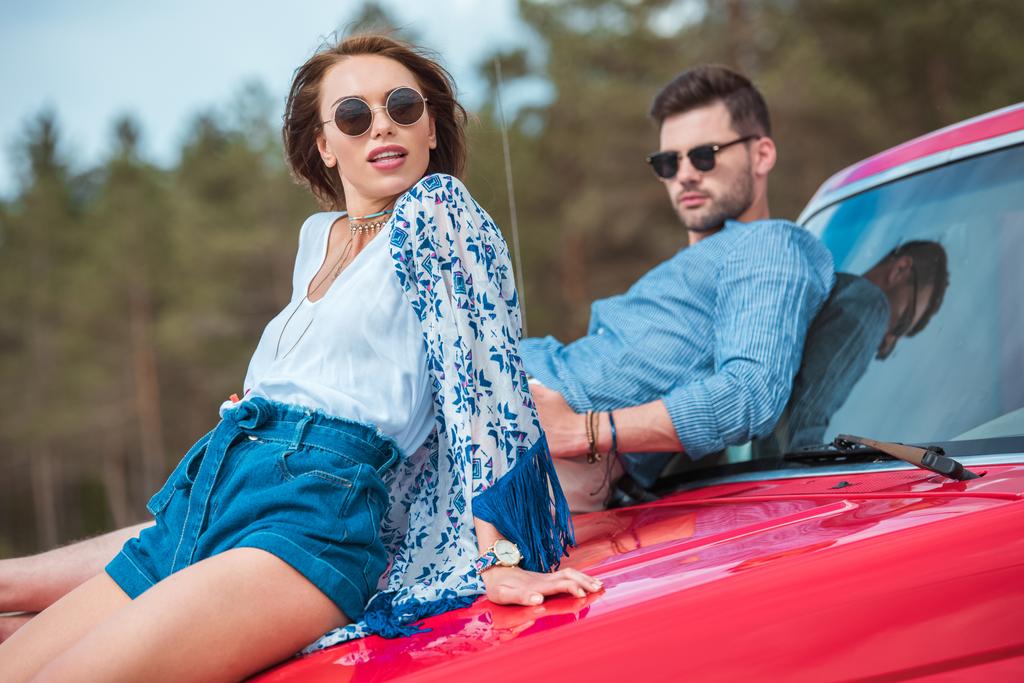 nuori tyylikäs pari aurinkolasit istuu punainen auto
  - Valokuva, kuva