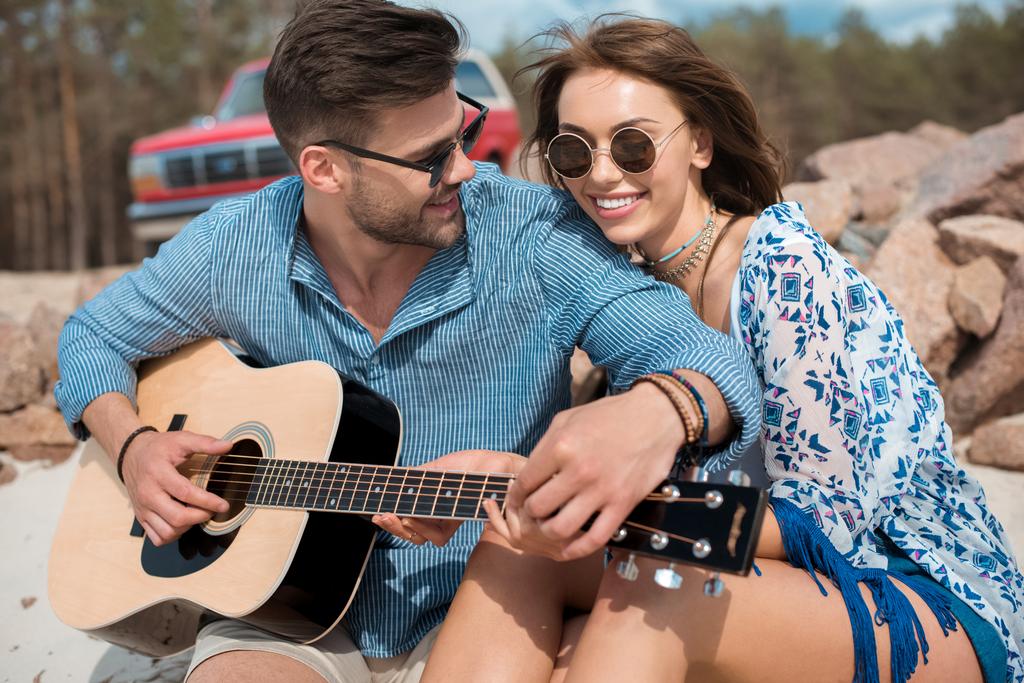 szczęśliwa para przytulanie gdy mężczyzna gra na gitarze akustycznej - Zdjęcie, obraz