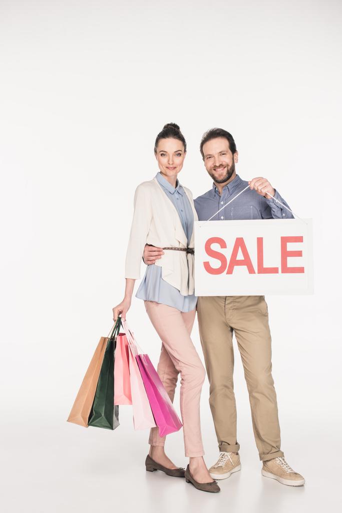 Lächelndes Paar mit Verkaufsbanner und Einkaufstaschen auf weißem Grund - Foto, Bild