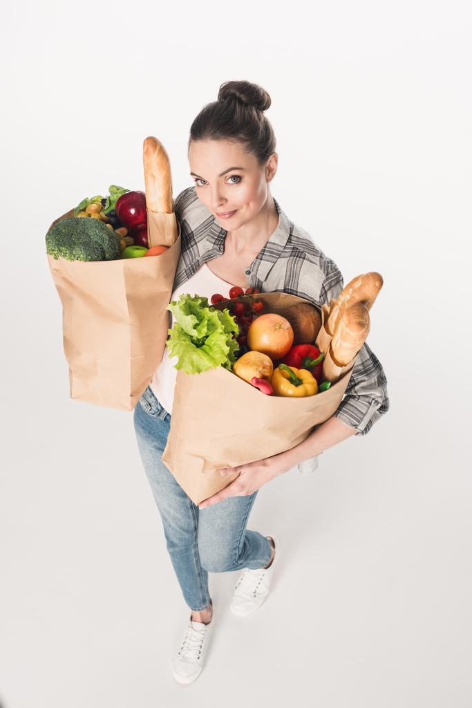 vista ad alto angolo della donna attraente che tiene pacchetti di carta con generi alimentari isolati su bianco
 - Foto, immagini