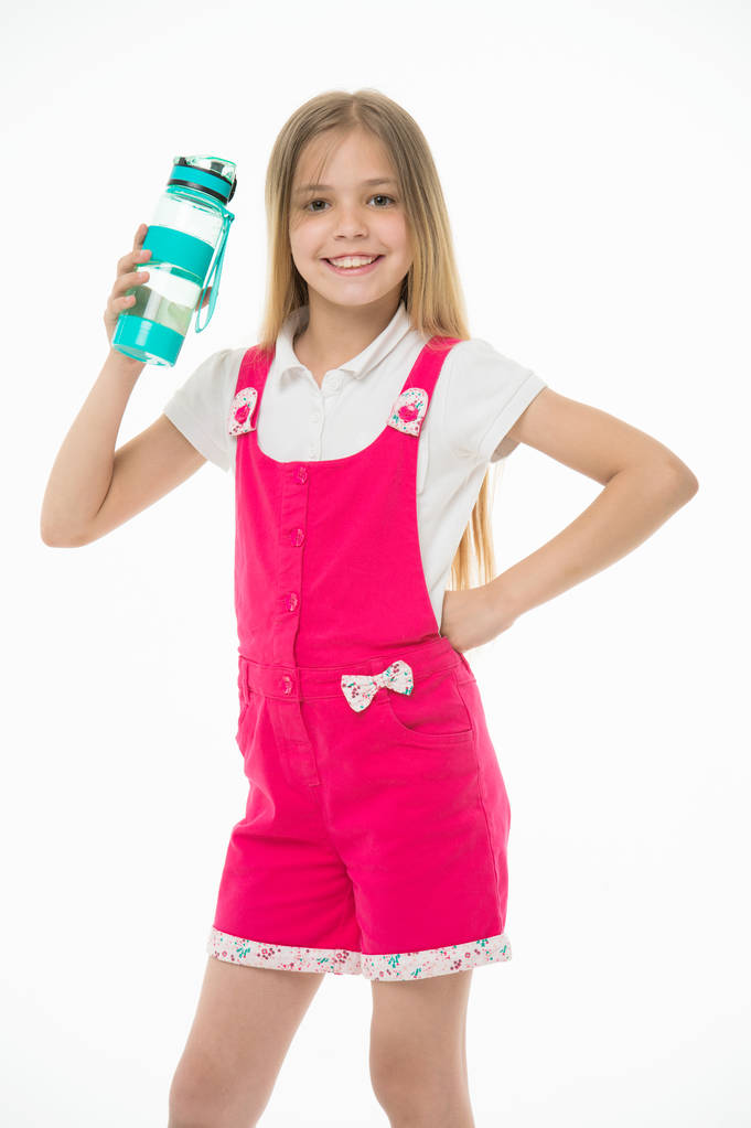 Счастливый ребенок в розовом комбинезоне держать бутылку воды. Маленькая девочка улыбается пластиковой бутылкой, изолированной на белом. Питьевая вода для здоровья. Жажда и обезвоживание. Детская деятельность и энергия
 - Фото, изображение