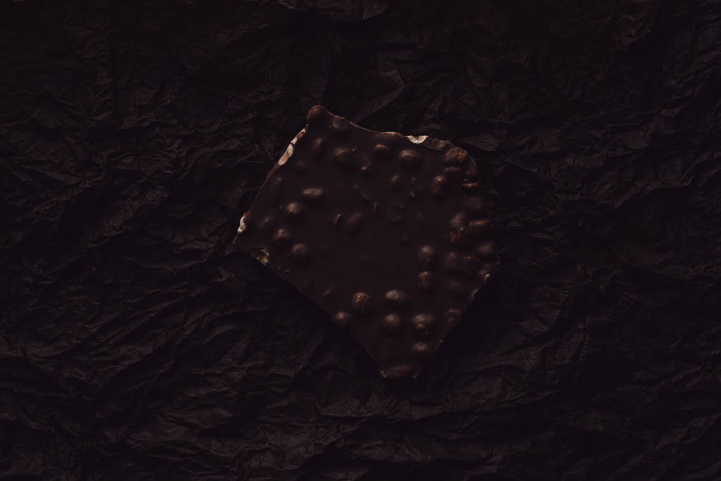 Ansicht von Schokolade mit Nussteilen auf Oberflächenbeschichtung durch schwarzes zerknülltes Papier  - Foto, Bild