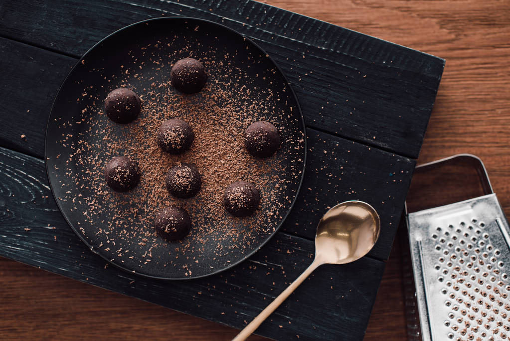 top view of cutting board with truffles on plate covering by grated chocolate, spoon and grater on wooden table - Photo, Image